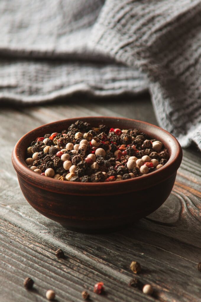 A rustic wooden bowl filled with colorful peppercorns on a wooden table, perfect for culinary themes.